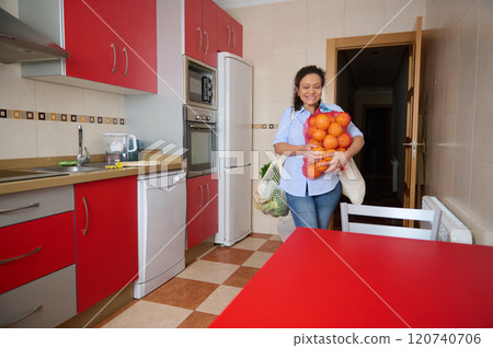 Smiling woman carrying oranges into her modern kitchen Smiling woman carrying oranges into her modern kitchen 120740706