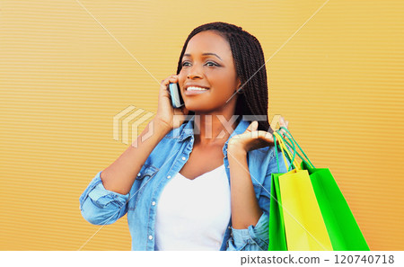 Fashion happy smiling african woman with shopping bags talking on phone on orange background Fashion happy smiling african woman with shopping bags talking on phone on orange background 120740718