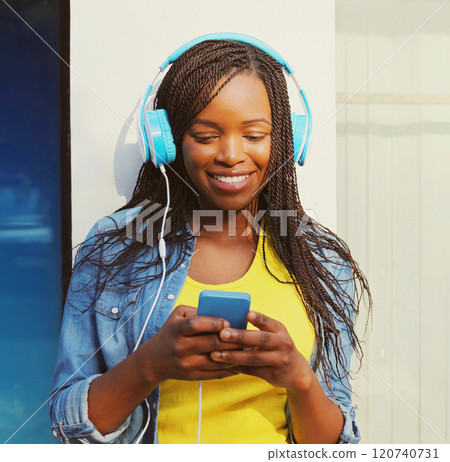 Fashion pretty smiling african woman with headphones listens to music using smartphone in the city Fashion pretty smiling african woman with headphones listens to music using smartphone in the city 120740731