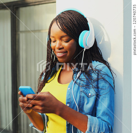 Fashion pretty smiling african woman with headphones listens to music using smartphone in the city Fashion pretty smiling african woman with headphones listens to music using smartphone in the city 120740735