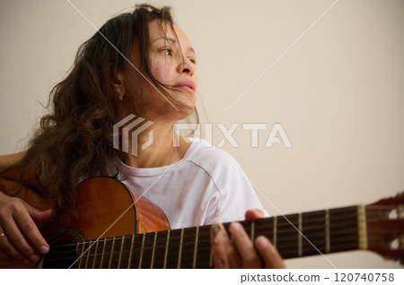 Woman in white shirt playing acoustic guitar thoughtfully indoors 120740758