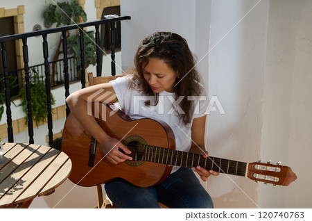 Woman playing acoustic guitar on sunny apartment balcony Woman playing acoustic guitar on sunny apartment balcony 120740763