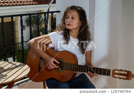 Woman playing guitar on a sunlit balcony enjoying the afternoon 120740764