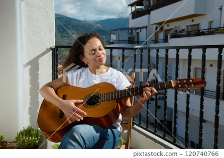 Woman enjoying playing guitar on a sunny balcony afternoon Woman enjoying playing guitar on a sunny balcony afternoon 120740766