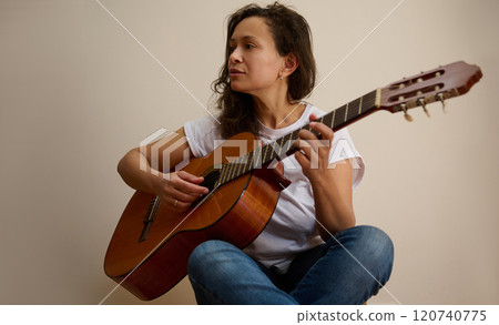 Woman playing acoustic guitar in relaxed home setting Woman playing acoustic guitar in relaxed home setting 120740775