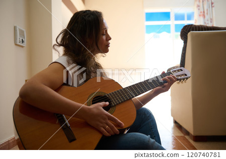 Woman playing acoustic guitar in cozy home setting 120740781