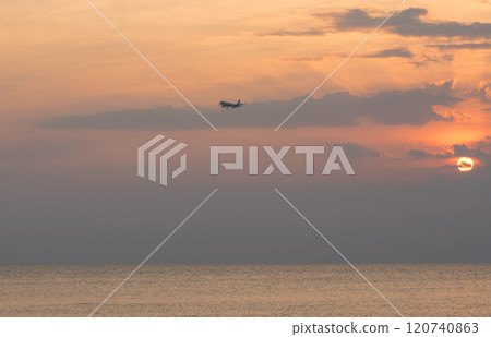 Airplane flying over the sea with a colorful sunset in the background 120740863
