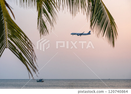 Tropical scene with an airplane flying over the sea at sunset, with palm leaves and a boat in the foreground Tropical scene with an airplane flying over the sea at sunset, with palm leaves and a boat in the foreground 120740864