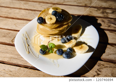 Stack of pancakes with bananas and blueberries on a white plate 120740894
