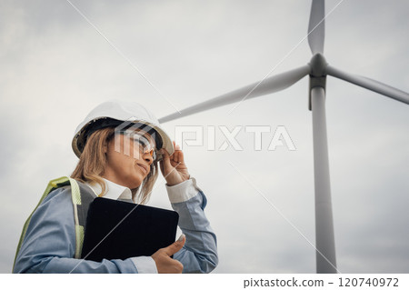 A dedicated female engineer is meticulously evaluating the performance of wind turbines at a cuttingedge renewable energy facility, ensuring efficiency and sustainability in energy production 120740972