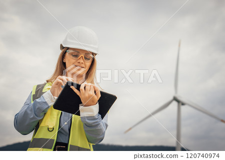 A dedicated female engineer is at a wind farm, using a tablet equipped with advanced technology to conduct thorough data analysis, showcasing innovation and a strong commitment to sustainability 120740974