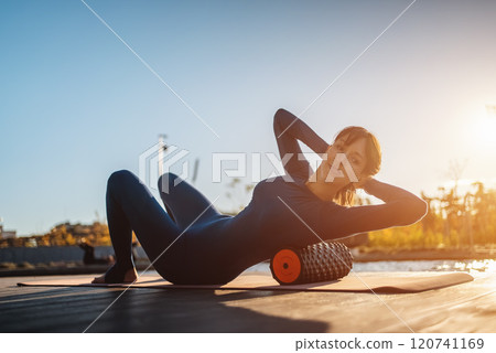 active fitness woman practicing muscular relaxation exercise with massaging foam roller, person stretching with fascial release equipment after sports training, back pain and body stiffness release 120741169