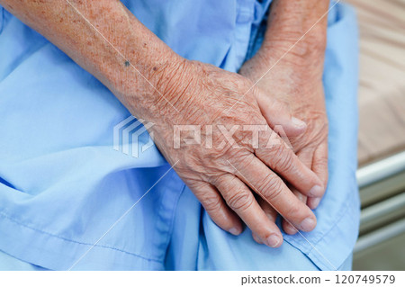 Asian elder senior woman patient sitting on bed in hospital, closeup at her hand. 120749579