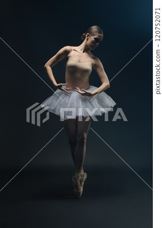 Graceful ballet dancer performing en pointe in a dark studio setting 120752071