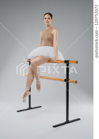 Ballerina practicing at barre in studio setting with neutral background Ballerina practicing at barre in studio setting with neutral background 120752072