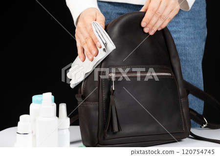 Cleaning the surface of a leather backpack with a cloth. Caring for leather accessories. Cleaning the surface of a leather backpack with a cloth. Caring for leather accessories. 120754745