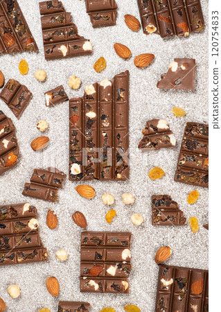 Broken chocolate pieces with nuts and raisins on a stone background top view Broken chocolate pieces with nuts and raisins on a stone background top view 120754833