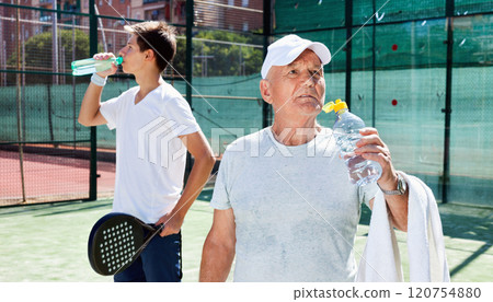 Padel players of different generations drink water on padel court 120754880