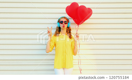 Happy young woman with red heart balloons listening to music in headphones on white background 120755184
