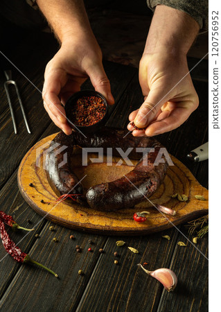 Hands carefully sprinkle spices onto a juicy dark blood sausage lying on a wooden board, surrounded by garlic and herbs, demonstrating the art of traditional cooking in a cozy kitchen Hands carefully sprinkle spices onto a juicy dark blood sausage lying on a wooden board, surrounded by garlic and herbs, demonstrating the art of traditional cooking in a cozy kitchen 120756952