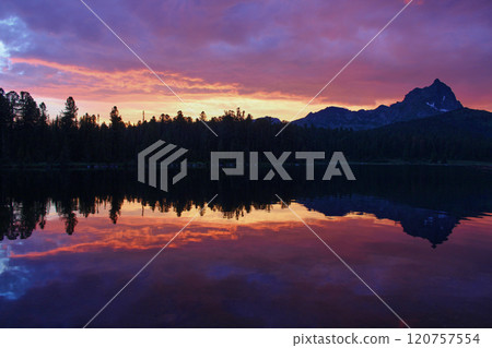 Incredibly beautiful sunset on mountain lake. Trees and a rocky peak reflected 120757554