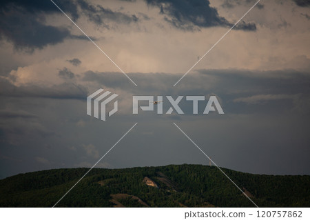 Clouds loom ominously as an airplane approaches the distant mountain range during twilight Clouds loom ominously as an airplane approaches the distant mountain range during twilight 120757862