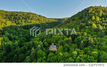 Nestled in natures embrace, a charming house surrounded by lush green hills at sunrise Nestled in natures embrace, a charming house surrounded by lush green hills at sunrise 120757972
