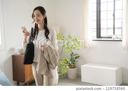 A woman preparing to go out indoors and looking at her smartphone A woman preparing to go out indoors and looking at her smartphone 120758560
