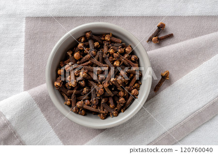 Whole clove buds in a bowl over gray textile background. 120760040