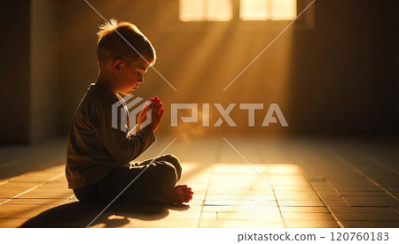 child sits on the floor, hands clasped together in prayer with sunlight streaming 120760183