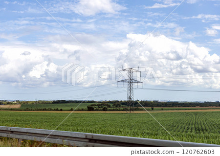 Electricity concept. High voltage power line pylons, electrical tower on a green field with blue sky. 120762603