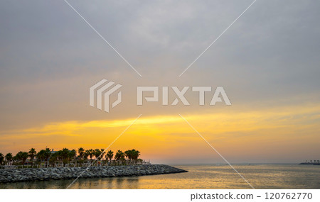 Sunset over the sea and palm trees in the distance on the shore. Sunset over the sea and palm trees in the distance on the shore. 120762770