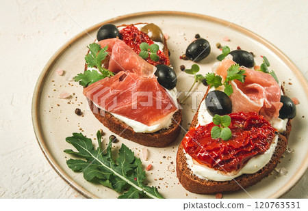 sandwiches with cheese and prosciutto, dried tomatoes and olives, breakfast on a plate, 120763531