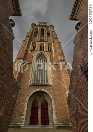 A majestic Gothic church under a dramatic cloudy sky. The intricate brickwork, towering windows, and clock tower reflect its historic architecture and timeless grandeur. A majestic Gothic church under a dramatic cloudy sky. The intricate brickwork, towering windows, and clock tower reflect its historic architecture and timeless grandeur. 120763726