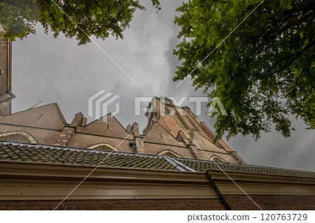 A majestic Gothic church under a dramatic cloudy sky. The intricate brickwork, towering windows, and clock tower reflect its historic architecture and timeless grandeur. A majestic Gothic church under a dramatic cloudy sky. The intricate brickwork, towering windows, and clock tower reflect its historic architecture and timeless grandeur. 120763729