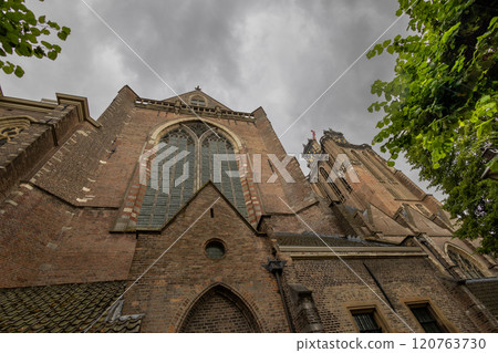 A majestic Gothic church under a dramatic cloudy sky. The intricate brickwork, towering windows, and clock tower reflect its historic architecture and timeless grandeur. A majestic Gothic church under a dramatic cloudy sky. The intricate brickwork, towering windows, and clock tower reflect its historic architecture and timeless grandeur. 120763730