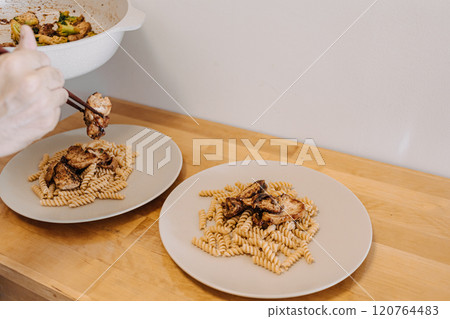 Man preparing two dishes of homemade pasta in his small kitchen. 120764483