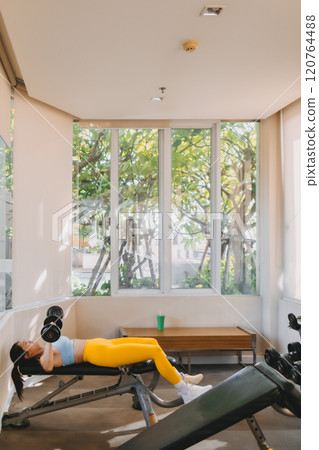 Woman in Blue Yellow outfit does Dumbbell Bench Press for chest workout. 120764488