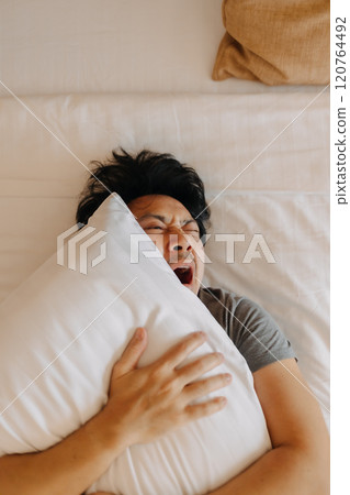 Sleepy man keep on sleeping on the bed, using pillow covering his face. Sleepy man keep on sleeping on the bed, using pillow covering his face. 120764492