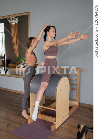 Engaging in a Pilates Training Session guided by the Instructor alongside the Client Engaging in a Pilates Training Session guided by the Instructor alongside the Client 120764870