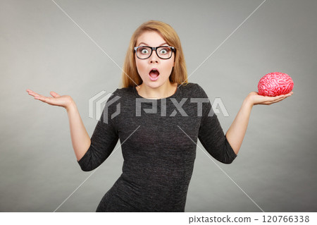 Woman in eyeglasses being confused holding brain 120766338