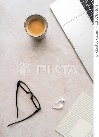 Minimal workspace with laptop, black glasses, coffee cup, wireless earbuds, and striped notebook on white desk Minimal workspace with laptop, black glasses, coffee cup, wireless earbuds, and striped notebook on white desk 120766672