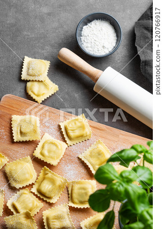 Homemade pasta ravioli with filling on wooden cutting board on dark background with flour, basil  120766917