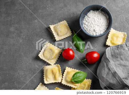 Flat lay of pasta ravioli with tomato and basil on dark background with flour and napkin. Flat lay of pasta ravioli with tomato and basil on dark background with flour and napkin. 120766919
