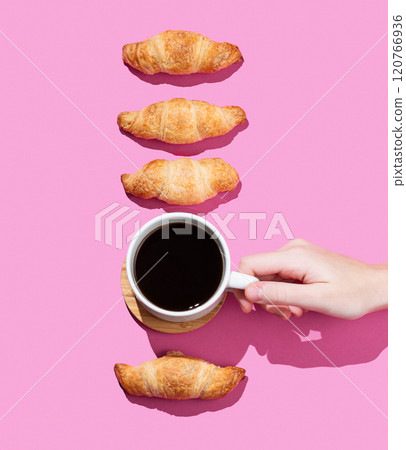 Hand holding a cup of espresso coffee on a pink background with shadow and fresh mini croissants. 120766936