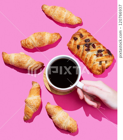 Hand holding a cup of espresso coffee on a pink background with fresh mini croissants Hand holding a cup of espresso coffee on a pink background with fresh mini croissants 120766937