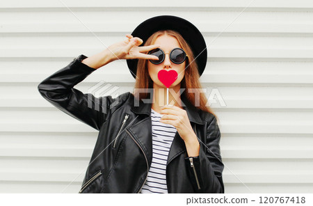 Cool young girl with red lollipop heart wearing fashion black hat leather jacket on white background 120767418