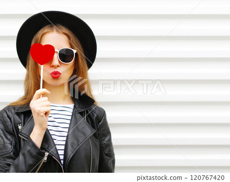 Fashion portrait young woman with red lips sending kiss with lollipop heart in black hat on white Fashion portrait young woman with red lips sending kiss with lollipop heart in black hat on white 120767420