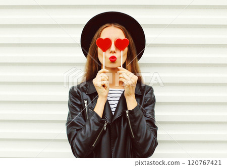 Fashion portrait sweet woman with red lipstick blowing kiss with lollipop heart in black hat, jacket Fashion portrait sweet woman with red lipstick blowing kiss with lollipop heart in black hat, jacket 120767421