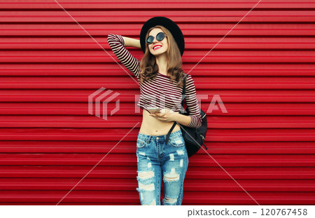 Portrait of stylish smiling young woman posing wearing a black round hat on a red background Portrait of stylish smiling young woman posing wearing a black round hat on a red background 120767458